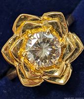 Close-up front view of ring showing central moissanite stone and flower petal design in gold tone.