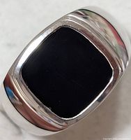 Close-up front top view of rectangular black onyx stone set in polished silver band ring.