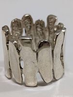 Close-up photo showing front side of silver ring with overlapping flat textured panels making a wide band.