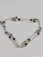 Silver necklace with multi-color gemstones laid flat to show length and gem placements