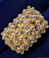 Close-up of broad silver band ring with multiple light yellow citrine stones clustered and secured with silver beads or prongs.