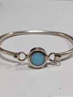 Front view of silver bangle bracelet with a round blue-green opal stone in the center, showing clasp loops on the sides.