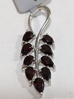 Close-up front view of silver pendant with deep red pear-shaped garnets arranged in two rows on curved silver stem forming leaf shape.
