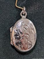 Closed view of the oval silver locket pendant showing the floral embossed front surface and bail for chain attachment.