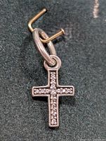 Close-up front view of a silver cross pendant with small stones embedded on the surface, hanging on a metallic thread.