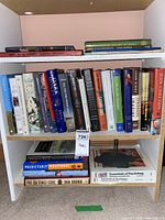 Bookshelf with assorted hardcover and paperback books including titles such as 'Predictably Irrational', 'The Da Vinci Code', and 'Essentials of Psychology'. Shelf itself not included.
