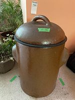 Front view of large brown ceramic container with lid, showing cylindrical shape and side handles