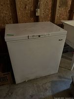 Front and side view of white Woods chest freezer in storage setting.