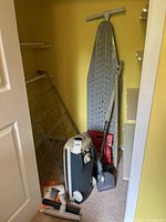 Electrolux Ambassador vacuum cleaner with hose, vacuum bags, and attachments along with drying rack and ironing board in corner