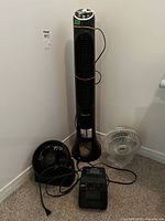 Photo of four items including a tall Honeywell Quiet Set tower fan, a small black portable fan, a small white fan, and a compact black heater on carpeted floor.