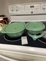 Large turquoise enamel covered warming dish and smaller Dutch oven with lids sitting on stove top, showing ware on warming dish lid.