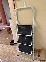 Full view of the foldable 3-step ladder showing its white metal frame and black steps