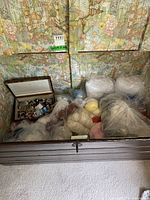 Open chest showing multiple plastic bags filled with knitting wool skeins and a wooden box containing buttons.
