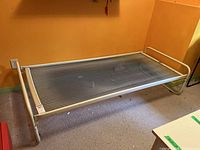 Metal cot bed frame against orange wall, showing full length and mesh surface