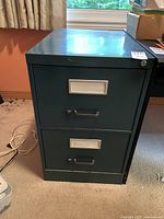 Front view of green two-drawer metal file cabinet showing both drawers closed with label holders and handles.