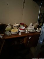 Wide view showing assorted plates, bowls, and decorative ceramic and glass pieces on wooden surface.