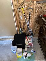 Overview photo displaying all items in the lot together in a garage space, including tools, paint supplies, garbage bags, and a floor mat.