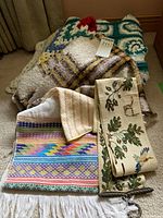 View of five various blankets and tapestries stacked together showing colors, textures, and patterns.