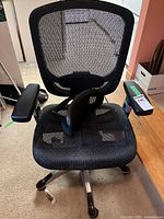 Front view of black mesh ergonomic office chair with armrests and caster wheels.