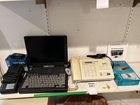 Photo showing the Compaq laptop, Brother fax machine, Magellan GPS in box, AlertMaster phone alert system in box arranged on a shelf.