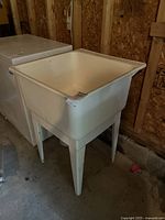 Full view of the white plastic laundry sink on legs showing general shape and size.