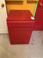 Front view of red wooden cupboard with closed door and drawer