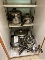 Shelved view showing several stacked stainless steel pots and pans with lids, including a steamer insert.