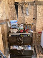 Overall view of lot showing drawers filled with tools and hardware, hand saws hanging on wall above, and sanding materials on top.