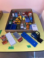 Top view of the lot showing multiple toy vehicles including the blue Tonka vehicle, Dinky trucks, and assorted smaller Hot Wheels and Corgi cars in a cardboard box.