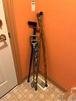 Three wooden walking sticks and one metal fold-out leaning seat with umbrella attachment leaning in corner by door