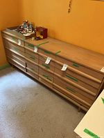 Full view of the wood dresser with 9 drawers, showing its overall shape, handles, and some contents on top that are not included.