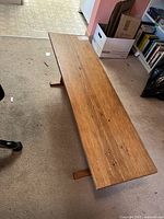 Top diagonal view of wooden bench on carpet showing length and wood grain surface.