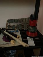 Photo showing metal bar xylophone with wooden frame, two plastic recorders, red and black megaphone, and music book on black surface.