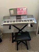 Full view of Yamaha DGX-205 keyboard on stand with stool underneath, showing keyboard keys, controls, music stand, and user manual on top.