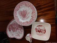Several pieces on table including round plates, heart-shaped dish, small pitcher, and square bowl with red patterns