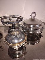 Overall view of the silver plate serving dishes showing two covered dishes and one handled serving bowl.