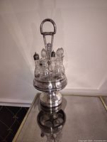 Full view of antique silver plated condiment set on a table showing stand with six glass bottles and central handle