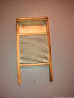 Front view of an antique wooden washboard with a ridged metal scrubbing surface and wooden legs, some faded printed text on the top wooden panel.