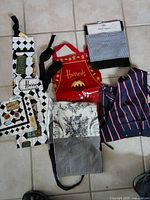 Photo shows six aprons laid flat on floor with various designs including Harrods and patterned fabrics.