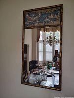 Full view of an antique Trumeau mirror with a carved wooden bamboo style frame and painted scene above the rectangular mirror.