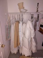Closet hanging with white cotton comforter, beige quilted blanket, and multiple white linens/sheets hanging on wire hangers, with some items on top shelf.
