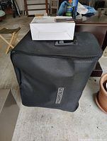 Black carry bag with handle and Frontgate logo, containing the camping cot mattress and frame.