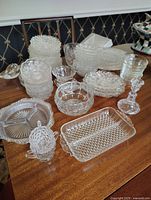 Wide view of assorted clear glass and crystal serving dishes, bowls, trays, and decorative items on a wood surface.