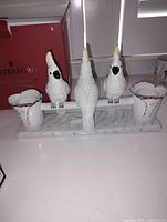 White ceramic cockatoo bird candle holder with three birds and two candle holders on marble-patterned base