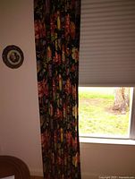 Drapes hanging beside a window partially closed, showing the full length and curtain rod attachment.