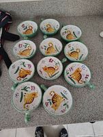 Ten green and white ceramic bowls laid out on a counter, each featuring an orange cat design with floral decorations.