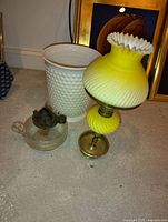 Photo showing three items: yellow opaline glass lamp with brass base, white hobnail vase with gold trim, and small clear glass kerosene lamp.
