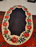 Full view of large oval latch hook rug with floral border placed on a patterned area rug.