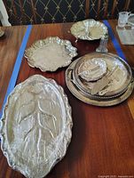Overview of all silver plate trays displayed on table including oval leaf design tray and several round trays.