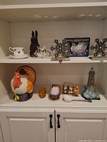 Shelf display of multiple holiday-themed vintage decor items including ceramic turkey, lamb figurine, blue rooster, snowflakes, sleigh box, teacup